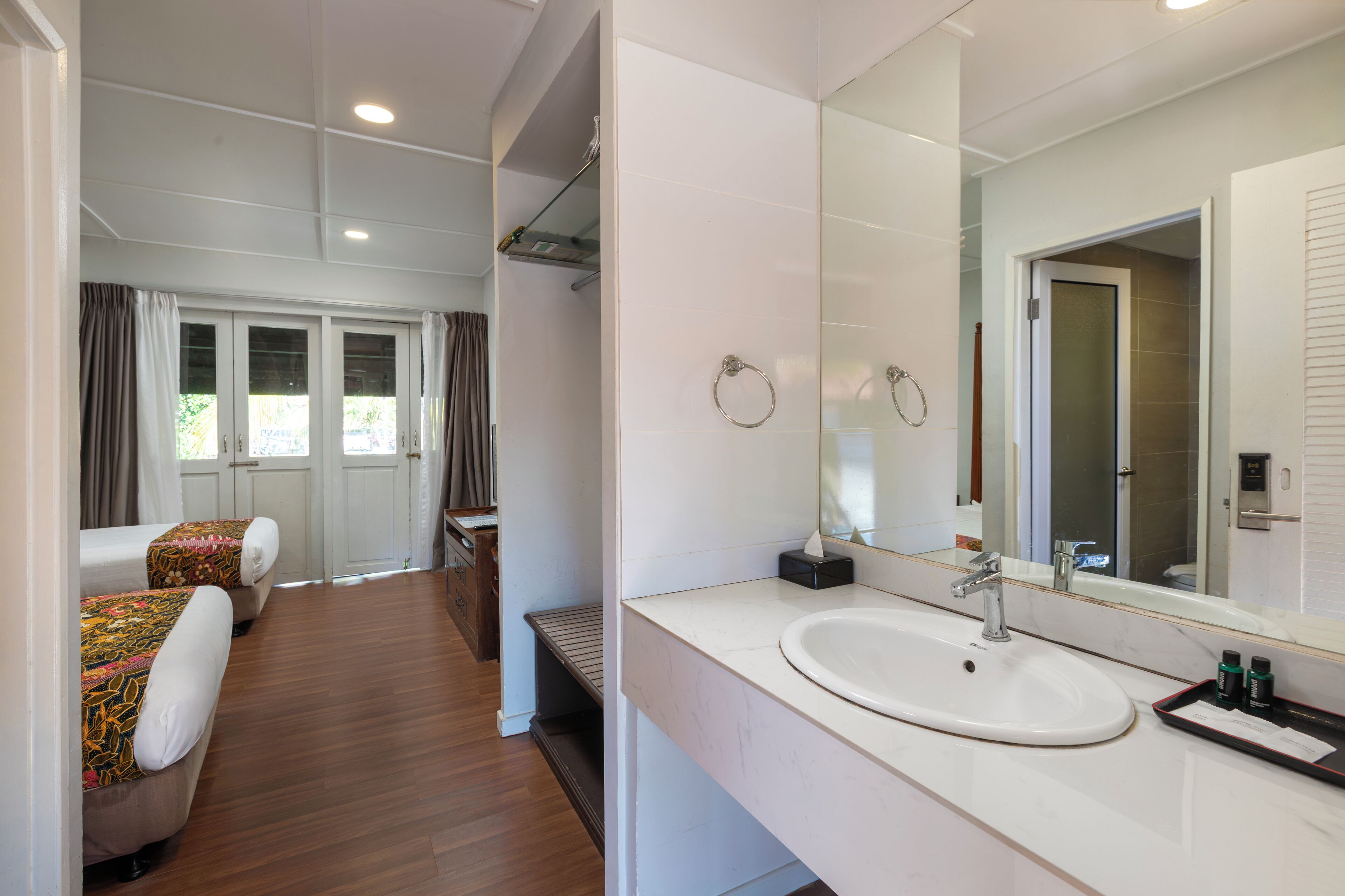 Une chambre d’hôtel avec un grand lit, une salle de bain avec un lavabo et un miroir, et une vue sur l’extérieur par la fenêtre.