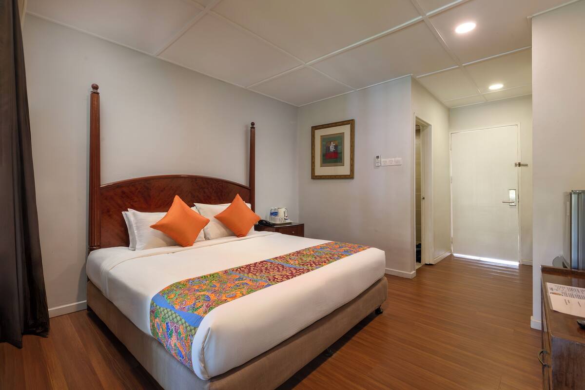 A hotel room with a large bed, wooden headboard, white bedding, and a colorful throw blanket.