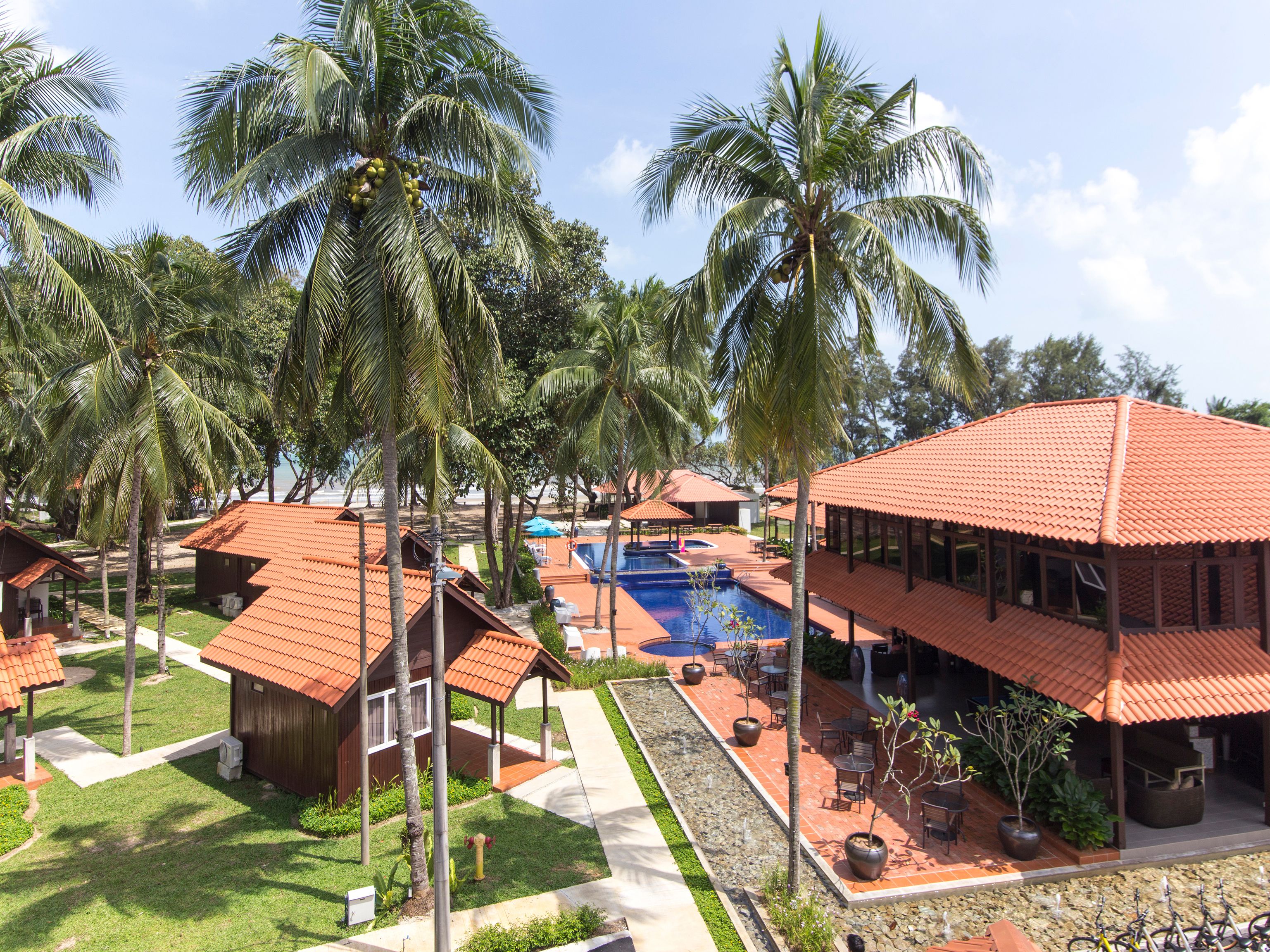 A resort with a swimming pool, palm trees, and red-roofed buildings.