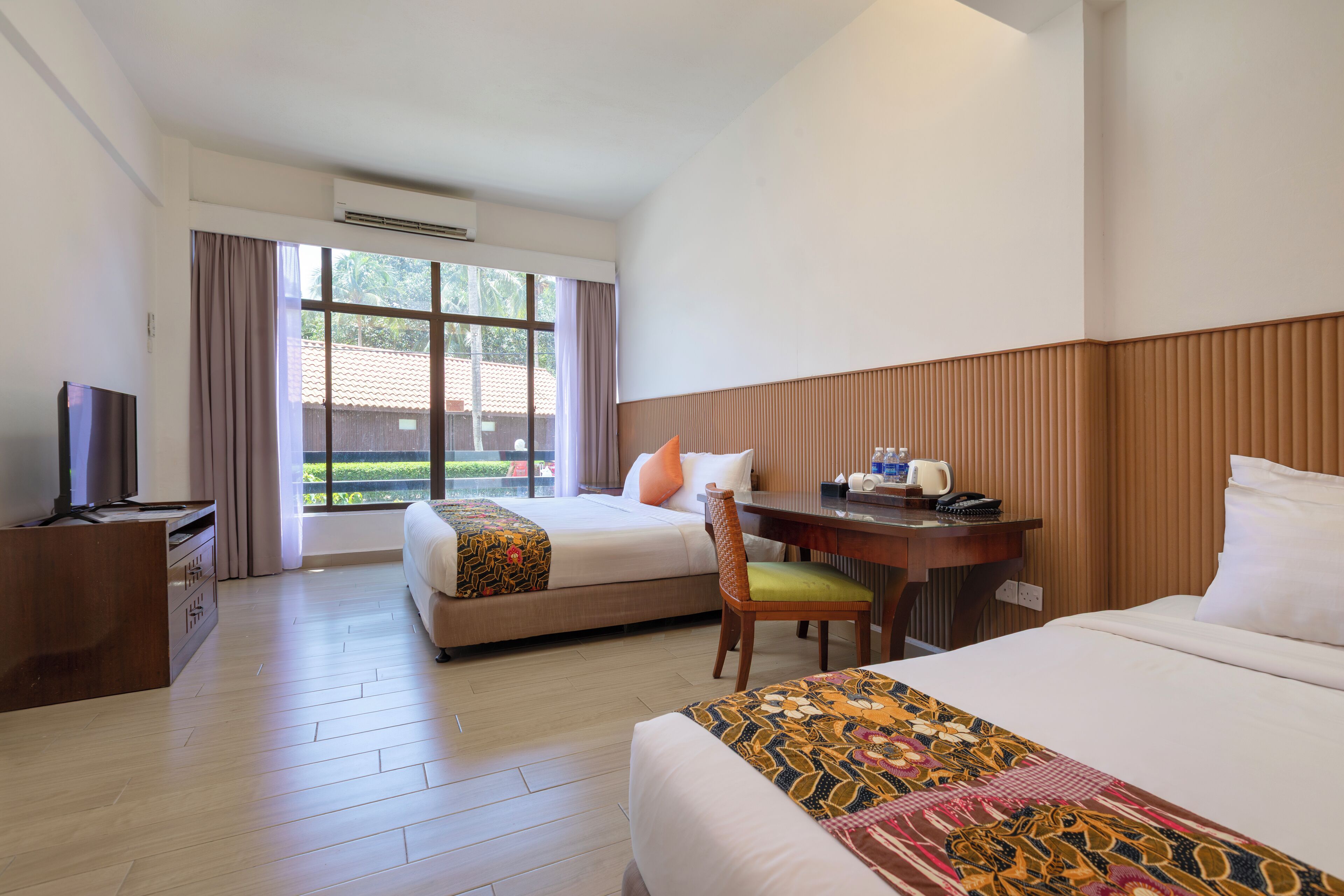 A hotel room with a bed, a desk with a chair, a television, and a window with curtains.