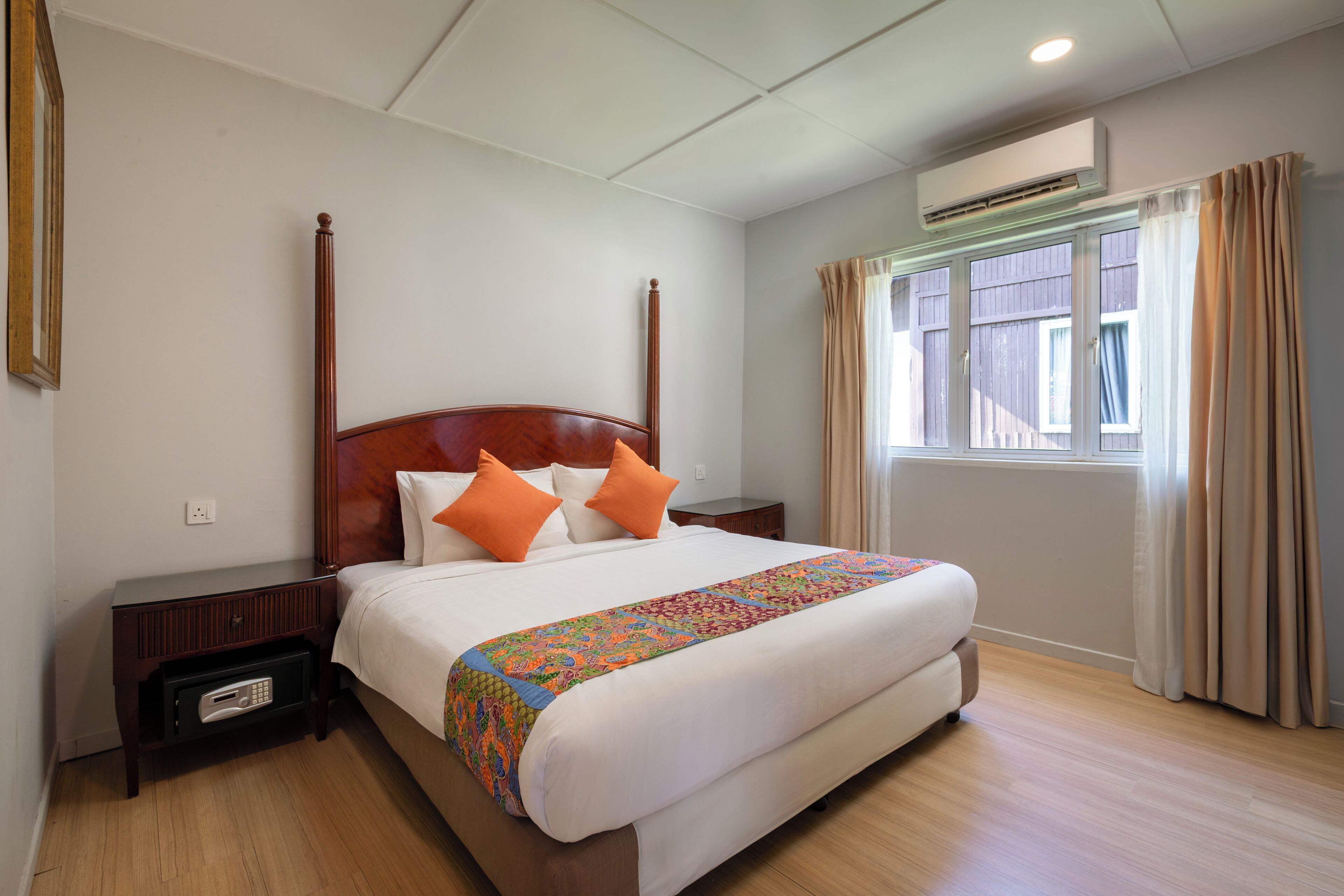 A neatly made bed with a wooden headboard, a bedside table with a radio, and a window with curtains.