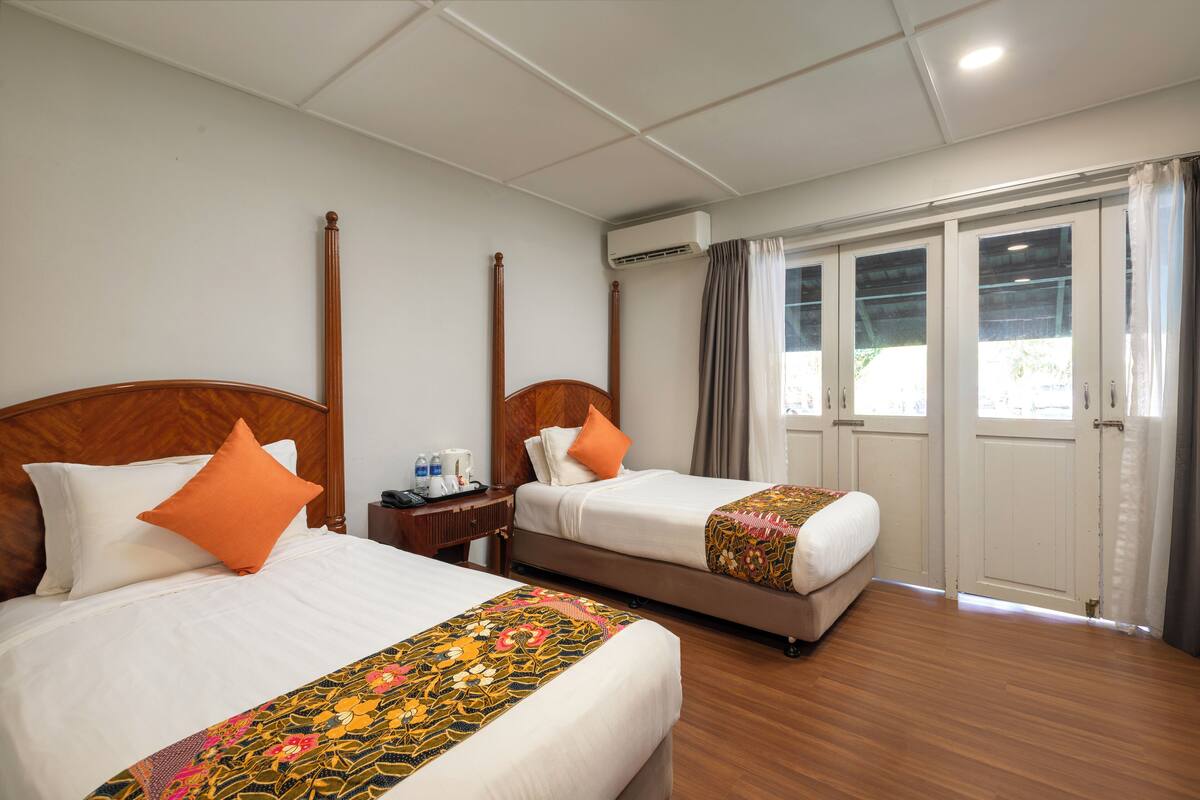 A hotel room with two beds, a wooden headboard, a nightstand, and a window with curtains.