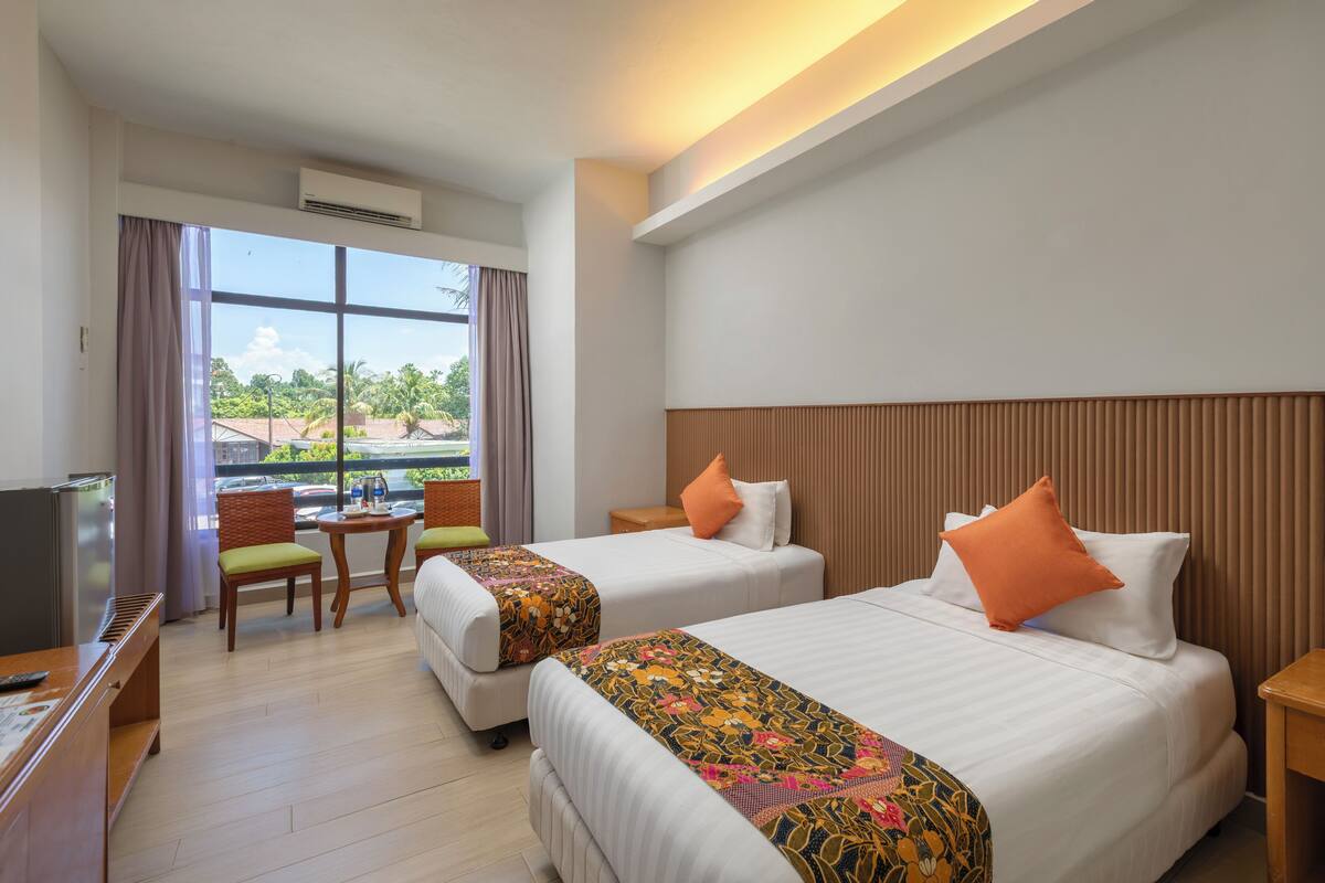 A hotel room with two beds, a desk, a chair, and a TV.