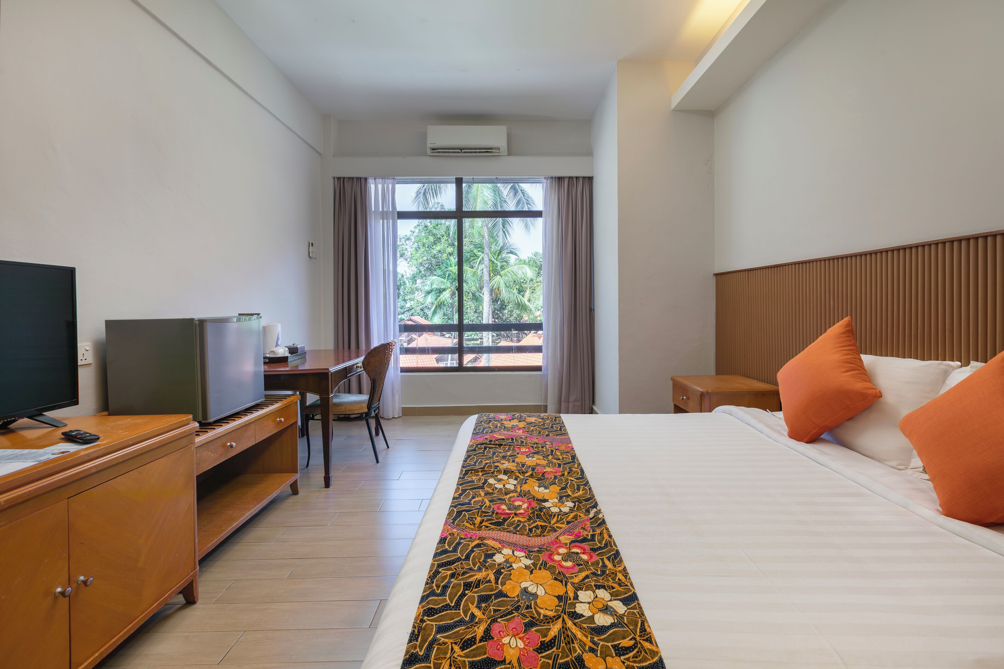 Una camera d'hotel con un letto, una scrivania con televisore, un comò e una finestra con tende.
