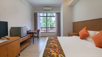 Una camera d'hotel con un letto, una scrivania con televisore, un comò e una finestra con tende.