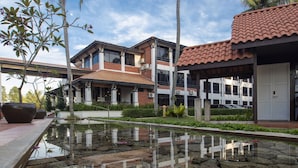 Een modern gebouw met een pannendak, een spiegelend waterkunstwerk en palmbomen.