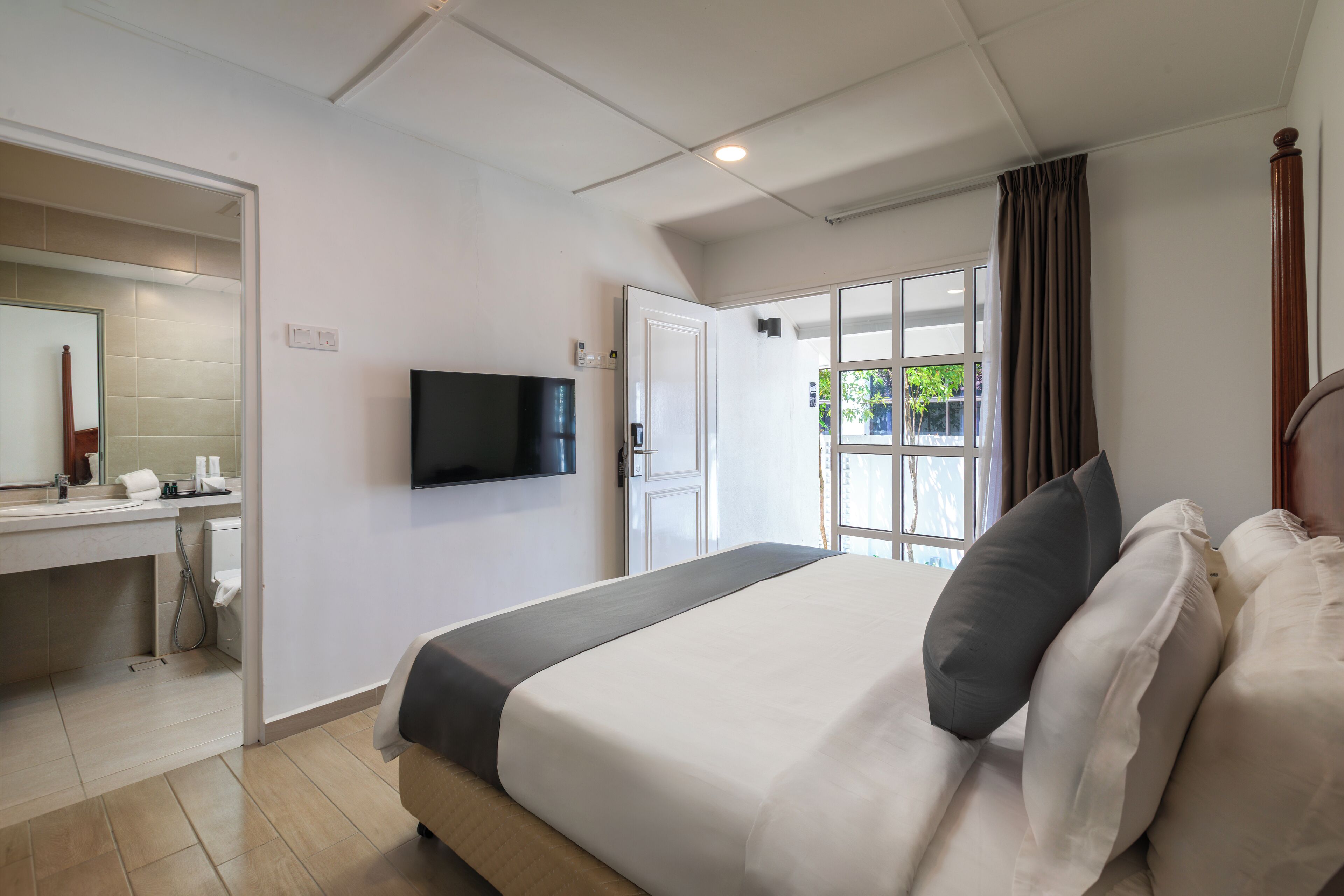 Quarto de hotel com cama, televisão, banheiro e janela com cortinas.