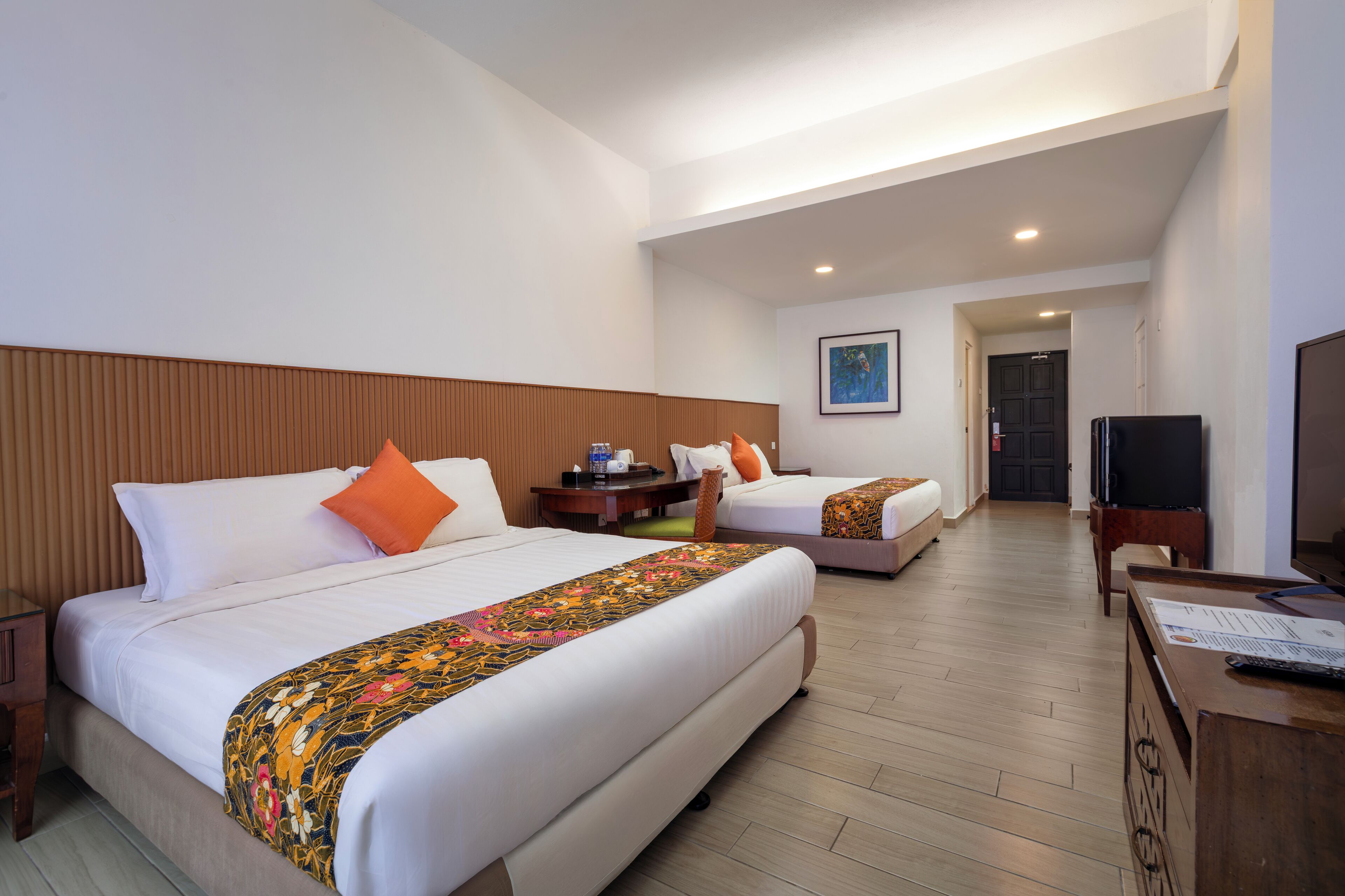 A hotel room with two beds, a television, a desk, and a door leading to another room.