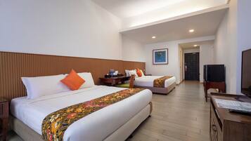 A hotel room with two beds, a television, a desk, and a door leading to another room.