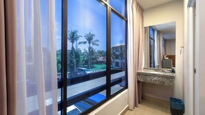 Een hotelkamer met grote ramen, een badkamer met een marmeren aanrecht en uitzicht op palmbomen en een straat.