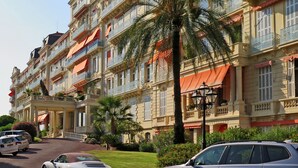 A multi-story hotel with balconies, palm trees, and a well-maintained lawn. - 1st Floor Apartment With Beautiful Sea View in Magnificent Character Building (Cannes)