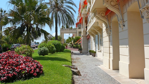 A hotel with a well-maintained garden, palm trees, and a pathway leading to the entrance. - 1st Floor Apartment With Beautiful Sea View in Magnificent Character Building (Cannes)