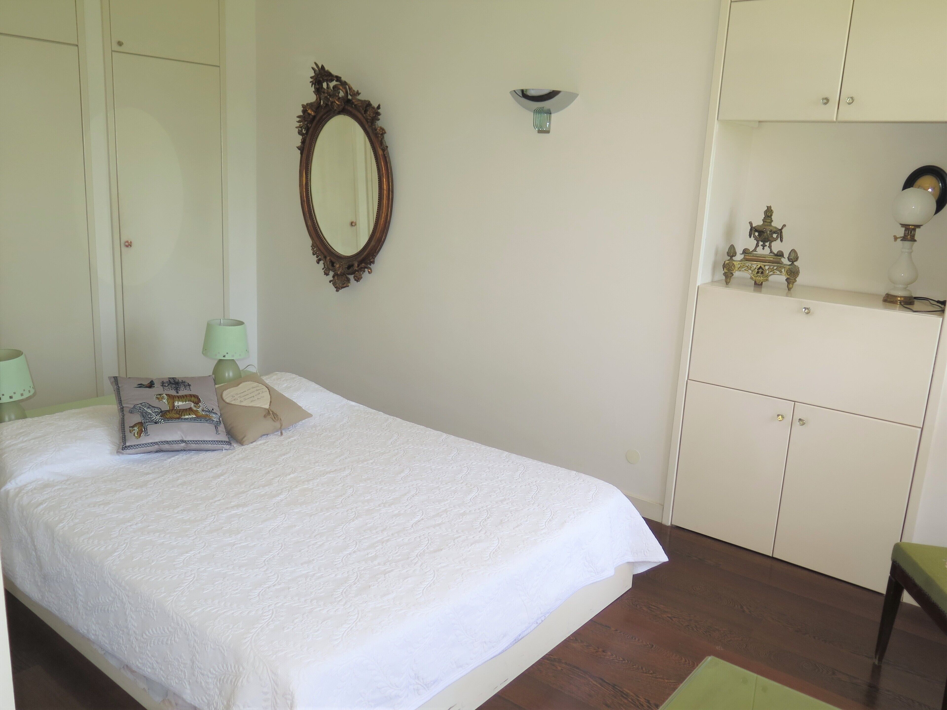 A bedroom with a bed, a dresser, a mirror, and a nightstand with lamps.