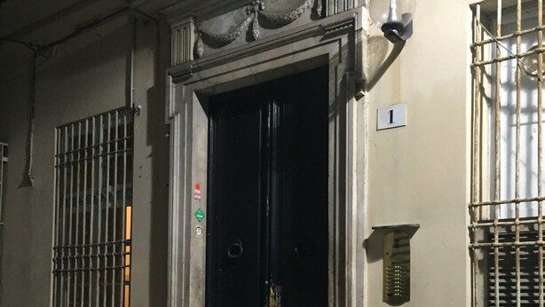 Ein Gebäudeeingang mit einer dunklen Tür und Stufen, die darüber hinaufführen, sowie vergitterten Fenstern.