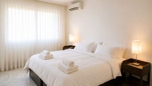 Une chambre d’hôtel comprenant un lit, deux tables de chevet avec des lampes, une fenêtre avec des rideaux et un appareil de climatisation.