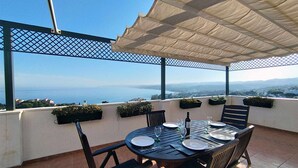 Une terrasse avec une table dressée pour le dîner, offrant une vue panoramique sur la mer et les montagnes lointaines.