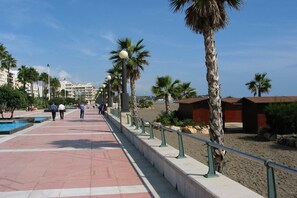 Eine Küstenpromenade mit Palmen, einem Schwimmbecken und einem Strandabschnitt.