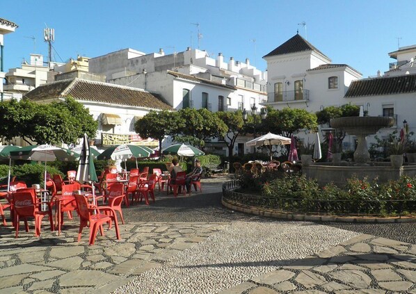 Zona de cafè a l'aire lliure amb cadires vermelles i ombrelles, paviment de pedra i una font.
