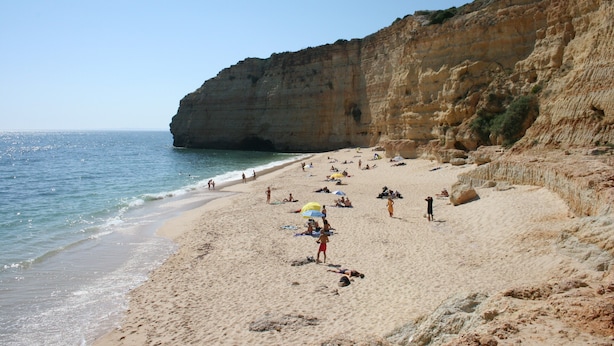 Une plage où des gens se détendent, un ciel dégagé et une falaise rocheuse.