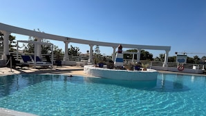 Une piscine d’un bleu éclatant, avec des chaises longues et une structure blanche au-dessus.