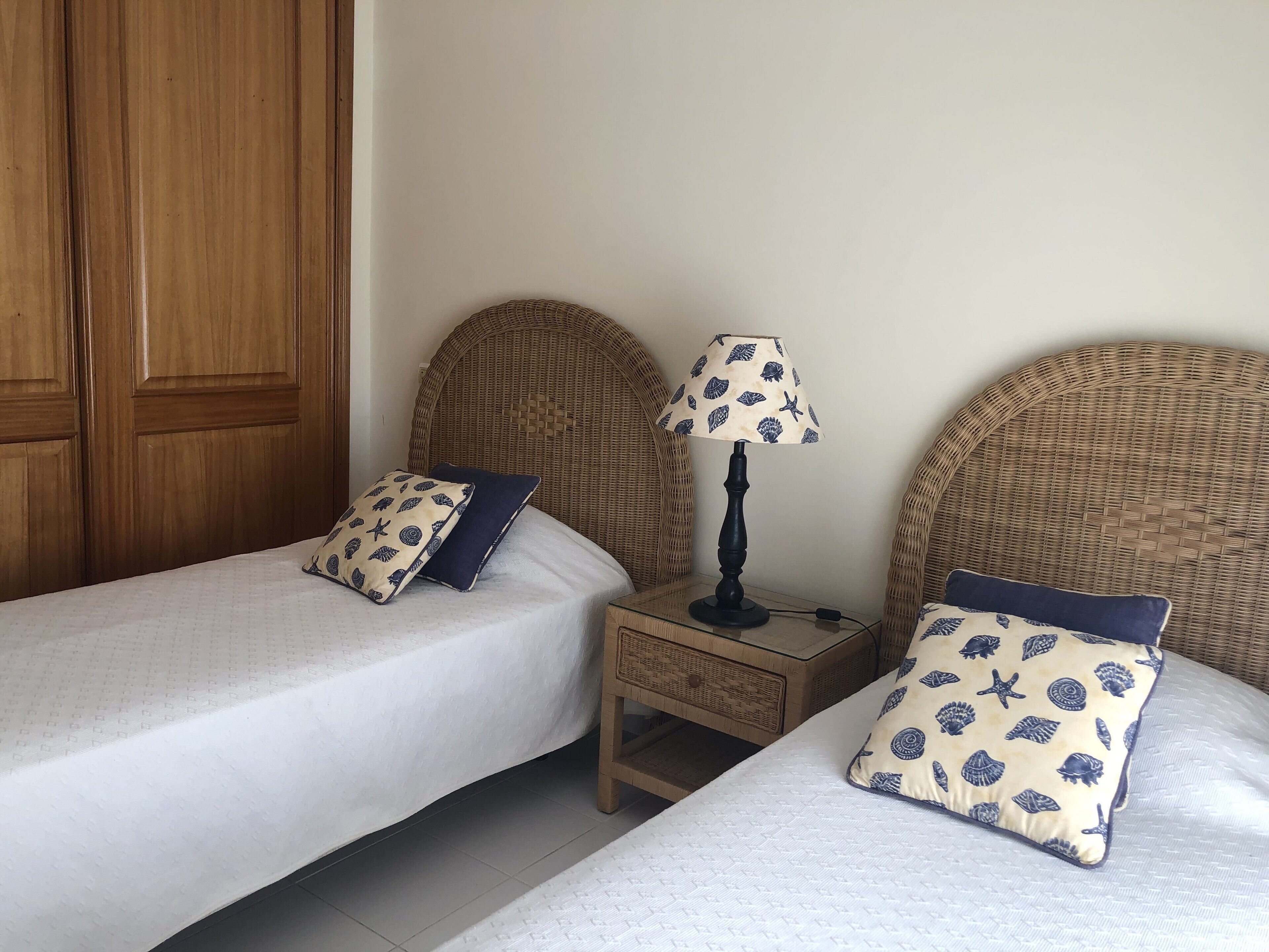 Een kamer met twee eenpersoonsbedden, elk met een passend kussen en een klein nachtkastje met lamp.