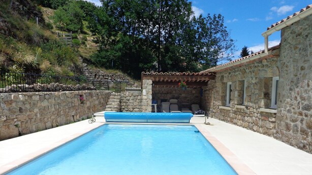 Une piscine rectangulaire, avec un mur en pierre d’un côté et une structure de toit en tuiles de l’autre.