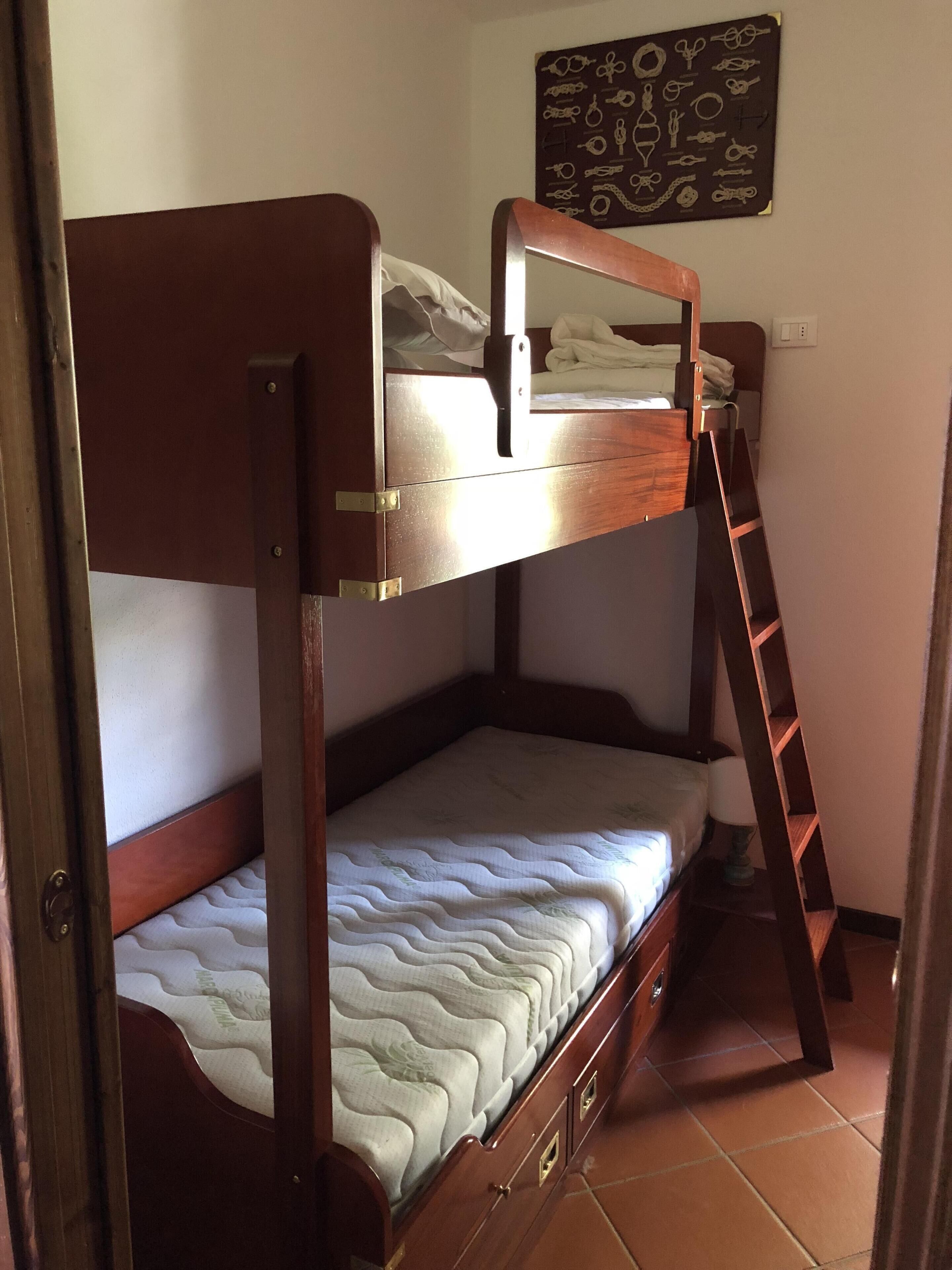 A bunk bed with a ladder, a small bedside table, and a wall decoration.