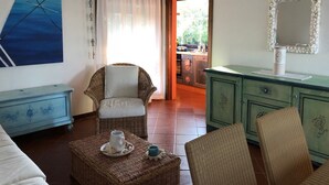 A cozy room with a wicker chair, a small table with a cup, a green cabinet, and a painting on the wall. - Punta Molara just 250 meters from the sea (San Teodoro)
