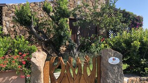 A stone wall with a wooden gate, surrounded by lush greenery and flowering plants. - Punta Molara just 250 meters from the sea (San Teodoro)