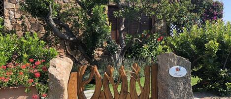A stone wall with a wooden gate, surrounded by lush greenery and flowering plants.