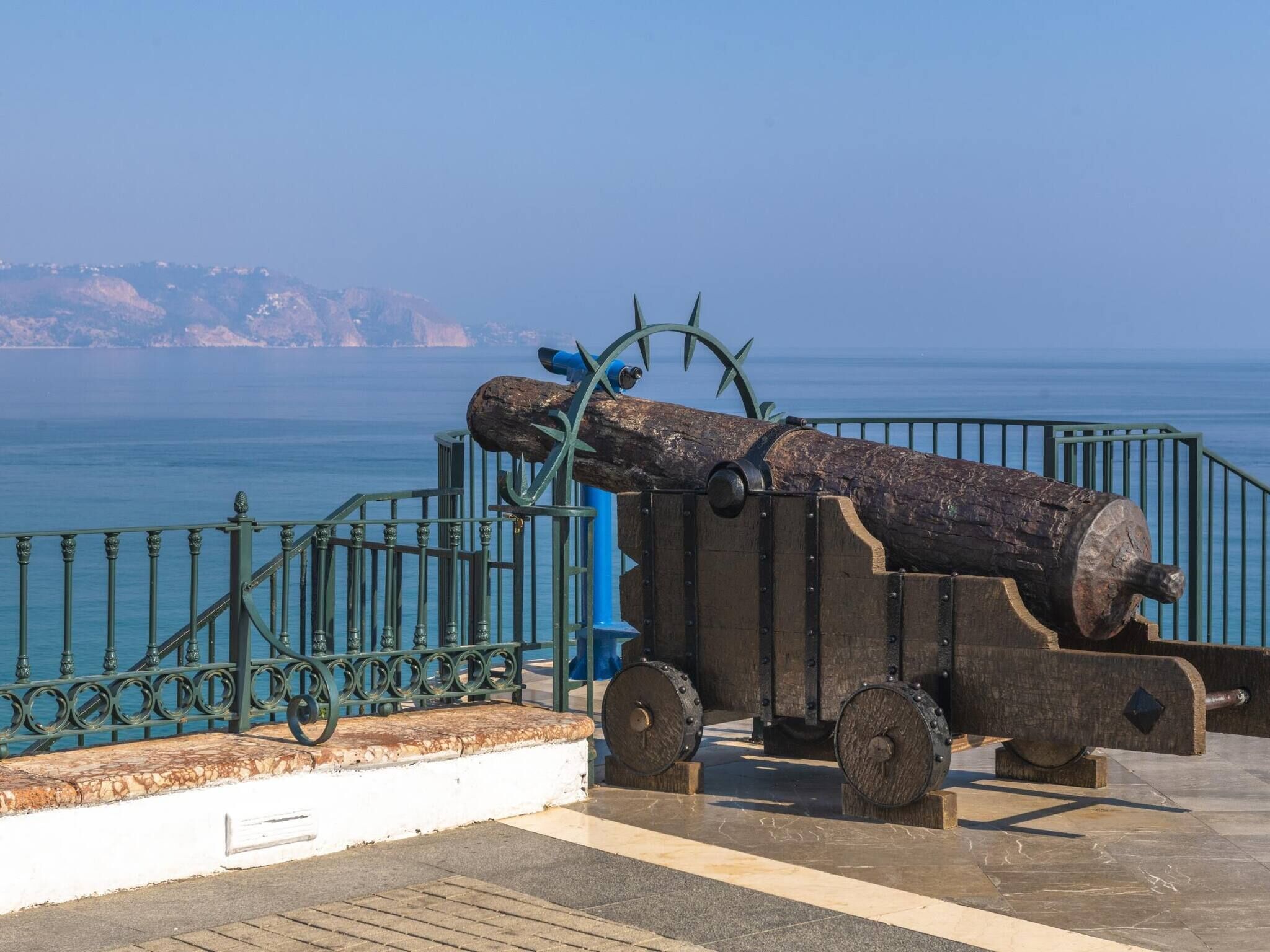 A cannon on display with a clear view of the sea and distant land in the background.
