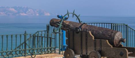 A cannon on display with a clear view of the sea and distant land in the background.