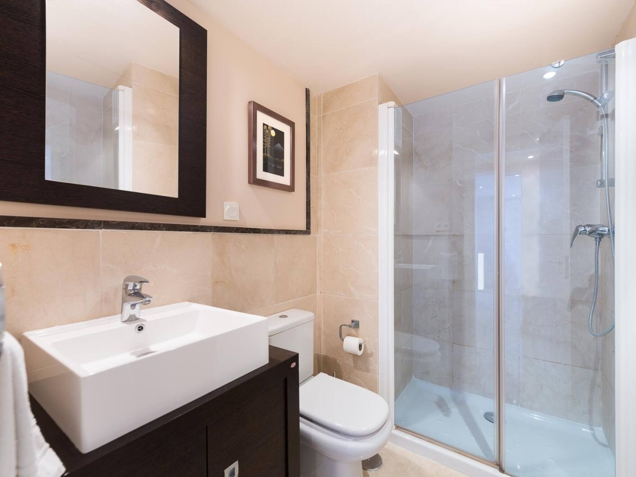 Un baño con lavamanos blanco, inodoro y ducha con mampara de vidrio.