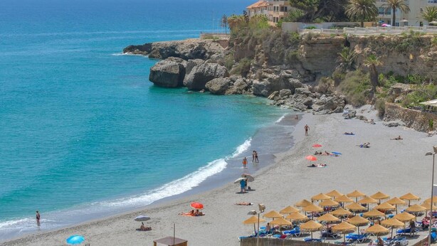 Una playa costera con aguas azul turquesa, acantilados rocosos y una hilera de sombrillas.