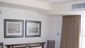 Un lit bien fait avec une tête de lit en bois, deux tableaux encadrés au mur, une fenêtre avec des rideaux et un plancher en bois.