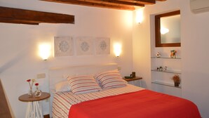 Une chambre à coucher avec un lit, des poutres en bois, des lampes fixées au mur et des étagères ornées d’objets décoratifs.