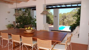 A dining area with a large wooden table and wicker chairs, a basket of fruit, and a view of a swimming pool. - This large, family-friendly house is very peaceful and has separate bedrooms. (Cala Saona)
