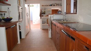 A kitchen with wooden cabinets, a stainless steel sink, and a tiled backsplash. - This large, family-friendly house is very peaceful and has separate bedrooms. (Cala Saona)