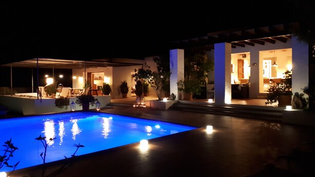 A poolside area with a pool, outdoor seating, and a building with illuminated windows. - This large, family-friendly house is very peaceful and has separate bedrooms. (Cala Saona)