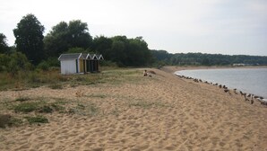 A sandy beach with a small wooden structure and a row of trees in the background.