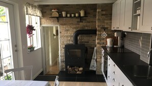 A kitchen with a brick wall, a wood-burning stove, white cabinets, and a black countertop.