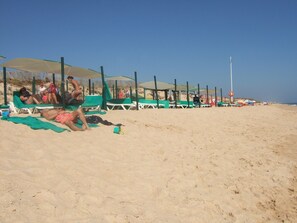 Een strand met rijen groene ligbedden en parasols, waarvan sommige door mensen worden gebruikt.
