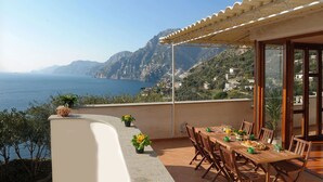 Una terraza con una mesa y sillas, con vistas a un paisaje costero con montañas y el mar.