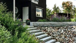 A modern two-story house with a black exterior, a balcony, and a stone pathway leading to the entrance. - Comfortable living in modern seaview house with rooftop terrace (Tyresö)