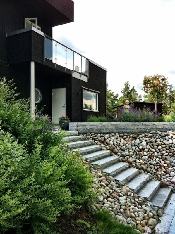 A modern two-story house with a black exterior, a balcony, and a stone pathway leading to the entrance.