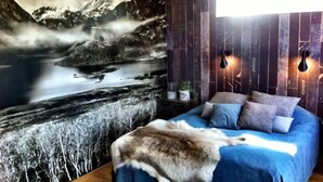 A bedroom with a mountain landscape mural, a bed with a blue blanket, and a fur throw. - Comfortable living in modern seaview house with rooftop terrace (Tyresö)