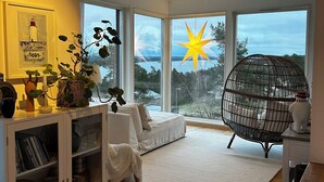 A modern living room with large windows, a white sofa, a hanging chair, and a star decoration. - Comfortable living in modern seaview house with rooftop terrace (Tyresö)