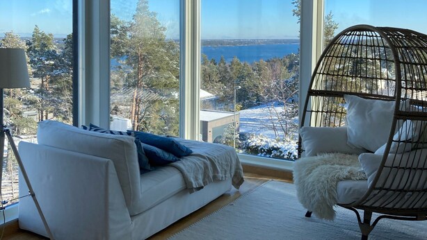 A modern room with large windows, a white sofa, a hanging chair, and a lamp. - Comfortable living in modern seaview house with rooftop terrace (Tyresö)