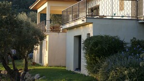 A two-story house with a balcony, a stone wall, and a garden with trees and shrubs. - Exceptional house in quiet magnificent view (Olmeto)