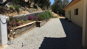 A gravel driveway leading to a building with a stone retaining wall and colorful flowers. - Exceptional house in quiet magnificent view (Olmeto)